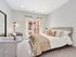 Elegant and bright bedroom with modern decor, plush carpeting, and floor-to-ceiling windows revealing a charming balcony view.