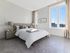 Bright, elegant bedroom with a plush bed, cozy decor, and sunlight streaming through large windows.