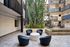 Modern apartment courtyard featuring sleek black seating around a circular table, with a striking tall cactus and elegant fountain waterfall as the centerpiece, surrounded by stylish balconies.