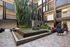 Modern apartment courtyard featuring stunning water feature, lush greenery, and chic seating area with colorful cushions.