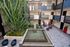 Stunning apartment courtyard featuring a modern water fountain, lush greenery, and inviting lounge chairs for relaxation.