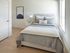 Bright and inviting bedroom featuring a plush bed with modern gray and white bedding, elegant artwork, and soft natural light streaming through large windows.