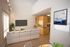 Bright and inviting living room with stylish sectional sofa, wall-mounted TV, and contemporary artwork, leading into a cozy kitchen with wood cabinetry and modern lighting.