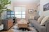 Bright and modern living room with a sleek gray sofa, chic wooden coffee table, and large TV, complemented by stylish wall art and a lush green plant.