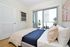 Bright and modern bedroom with large window, offering a stunning city view and access to a cozy balcony. Luxurious linens adorn the bed, complemented by contemporary artwork.