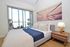 Bright bedroom with modern decor, featuring a comfortable bed with stylish cushions, a wooden nightstand with a lamp, and a serene balcony view through large glass doors.