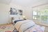 Bright and airy bedroom featuring a cozy modern bed, stylish artwork, and a large window with verdant views.
