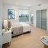 Bright and modern bedroom featuring a cozy bed, stylish artwork, and sliding closet doors, with a view of the outdoors through large windows.