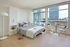 Modern bedroom with natural light featuring a comfortable bed, stylish decor, and a chic dining area with city skyline views.