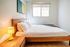 Bright and cozy bedroom boasting a sleek wood bed frame, modern art, natural light, and a warm ambiance with a stylish bedside lamp.