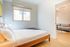 Bright and inviting bedroom with a sleek bed, cozy pillows, and a large window offering natural light, seamlessly connected to a stylish living room with elegant decor.