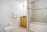 Bright, modern bathroom featuring sleek tile, a stylish granite vanity, and a glass shower door.