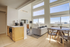 Bright and modern living area featuring a sleek kitchenette, cozy sofa, stylish dining table, and expansive windows offering stunning views.