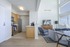 Bright and modern open-plan living space featuring a sleek kitchen with wooden cabinetry and stainless steel appliances, cozy living area with a chic gray armchair, and a large window providing ample natural light.