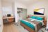 Modern bedroom with stylish wooden furniture, featuring a cozy bed with teal accents, a sleek workspace, and an open closet.