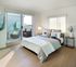 Bright and airy bedroom with stylish decor, featuring a cozy bed and a private balcony with comfortable seating and city views.
