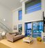 Modern apartment living room featuring sleek furniture, large windows with cityscape views, and a glass-railed staircase for a chic aesthetic.