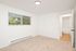 Bright and spacious bedroom with plush carpeting, large window with blinds offering a garden view, and an inviting doorway leading to an adjoining room.
