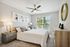 Elegant bedroom with modern decor, plush bedding, and large sunlit window, ideal for peaceful living.