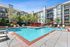 Inviting apartment complex featuring a sparkling pool with red umbrellas and lounge seating, surrounded by lush greenery and modern architecture.