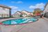 Inviting apartment complex with refreshing pool, modern lounge chairs, and vibrant red umbrellas set against a clear blue sky.