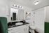 Modern bathroom with elegant fixtures, featuring a sleek black granite countertop, white vanity, and stylish artwork above the toilet.