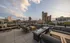 Inviting rooftop terrace with modern seating, cozy fire pits, and stunning urban skyline views under a picturesque sky.