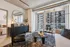Stylish urban apartment living room with modern decor, large windows, and a view of city architecture. Features cozy seating, a sleek coffee table, and a decorative mirror.