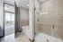 Modern bathroom with sleek glass shower, inviting bathtub, and a view to a bright bedroom with cityscape balcony access.