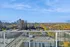 Stunning high-rise view from a modern apartment balcony overlooking a vibrant cityscape and lush greenery under a clear blue sky.