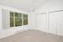 Bright and inviting bedroom with large window view of lush greenery, featuring ample closet space and soft carpet flooring.