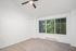 Bright and inviting room with plush carpet, large window offering scenic views, and a modern ceiling fan.