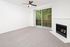 Bright and inviting living room with plush carpeting, a cozy fireplace, ceiling fan, and large sliding glass doors leading to a serene patio with lush green views.