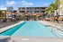 Luxurious apartment complex featuring a sparkling outdoor pool, modern lounge chairs, and lush palm trees under a clear blue sky.