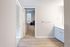 Bright apartment hallway featuring modern flooring, leading to a cozy carpeted bedroom with natural light.
