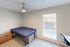 Cozy bedroom with a modern design, featuring a comfortable bed, stylish wooden nightstand, large window with blinds, and a sleek desk area.