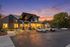 Charming building exterior at sunset with modern architecture, warm lighting, and ample parking in a serene setting.