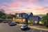 Charming modern building with large windows and a sleek design under a beautiful sunset sky, surrounded by lush greenery and ample parking space.