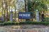 Charming entrance of ReNew Tallahassee with a welcoming stone sign framed by lush greenery and mature trees.