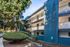 Charming multi-level blue apartment building with modern railings, nestled among lush greenery and a well-maintained landscape.