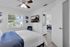 Charming bedroom with modern ceiling fan, large window view, and cozy white bedding, leading into a stylish living area and equipped with an in-unit laundry for convenience.