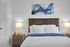 Inviting bedroom with cozy white bedding and plush pillows, accented by elegant bedside lamps and modern abstract art.