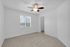 Bright and airy bedroom with plush carpet, large window, ceiling fan, and walk-in closet entrance.