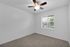 Bright bedroom with plush carpet, ceiling fan, and large window for natural light.