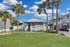Charming coastal apartment building with palm trees, a manicured lawn, and inviting porch under a vibrant blue sky.
