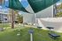 Outdoor fitness area with modern exercise equipment, palm trees, and lush greenery, perfect for an active lifestyle in a serene apartment complex setting.