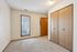 Cozy bedroom featuring soft carpeting, warm wood accents, natural light streaming through a large window, and ample closet space with wooden doors.