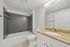 Modern bathroom with sleek granite countertop, large mirror, and elegant tiled bathtub.