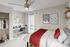 Modern bedroom with cozy bed, vibrant red accents, and sleek workspace featuring a minimalist desk and chair. Elegant wall art and warm natural light add charm.