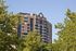 Elegant brick apartment building surrounded by lush green trees, against a clear blue sky.